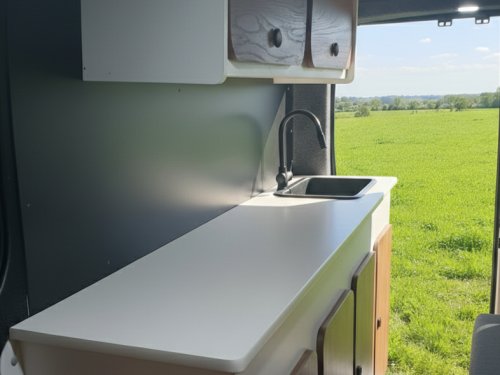 Kitchenette moderne de van aménagé avec plan de travail blanc et vue sur la nature.