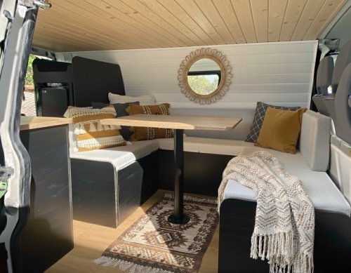 Aménagement intérieur de van : salon style bohème avec table en bois et banquettes.