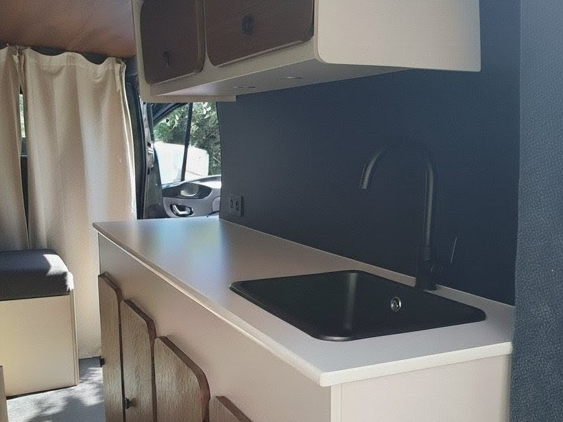 Cuisine de van aménagé au design minimaliste avec évier noir et finitions bois.