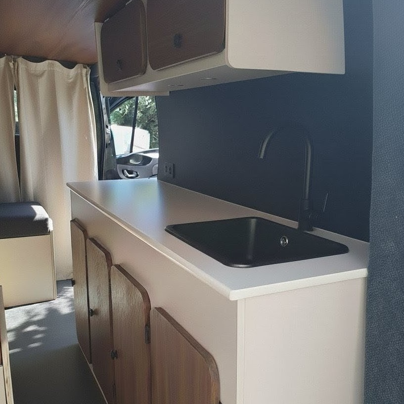 Cuisine moderne de van aménagé avec évier noir, plan blanc et façades en bois.
