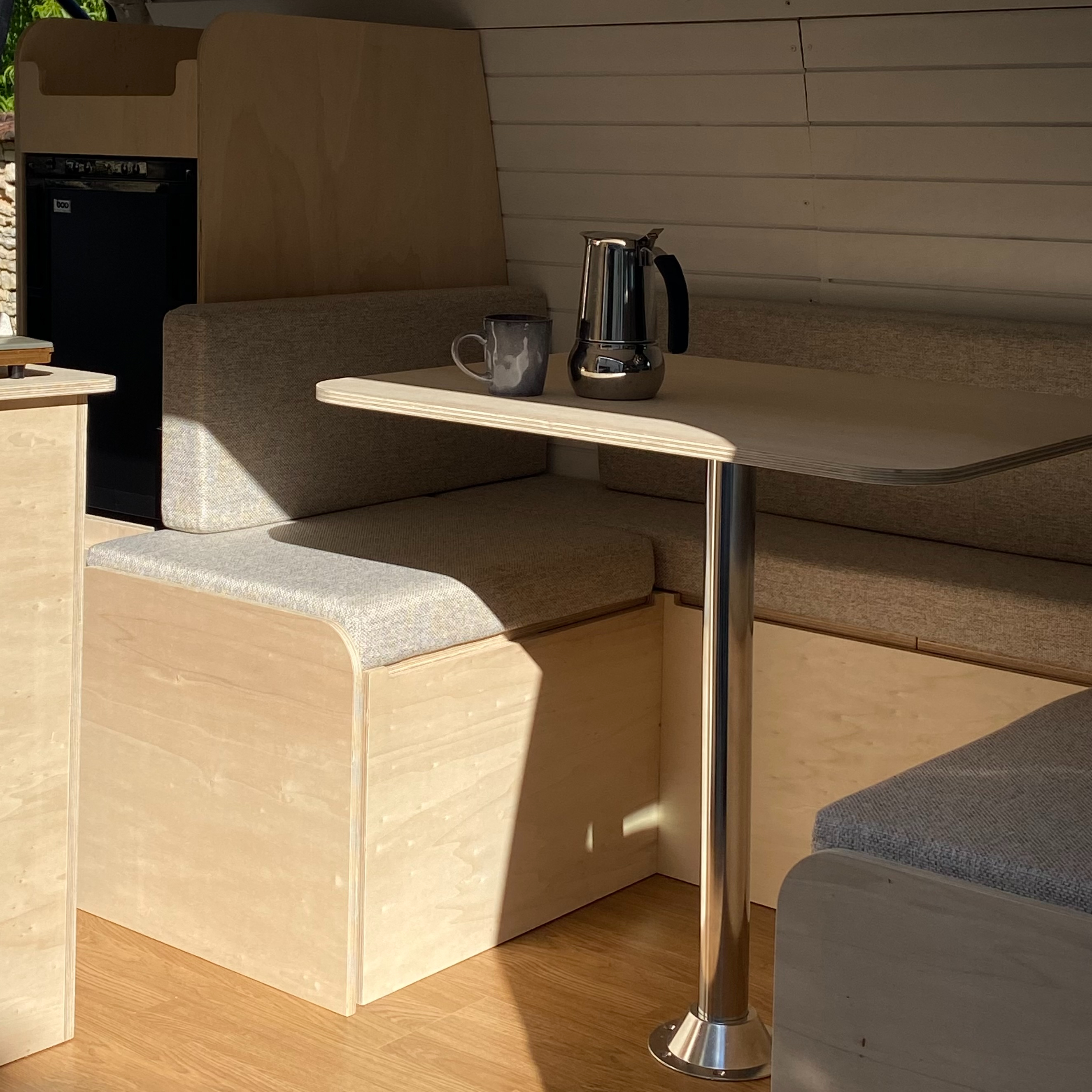 Intérieur de van aménagé minimaliste en bois clair avec coin repas ensoleillé.