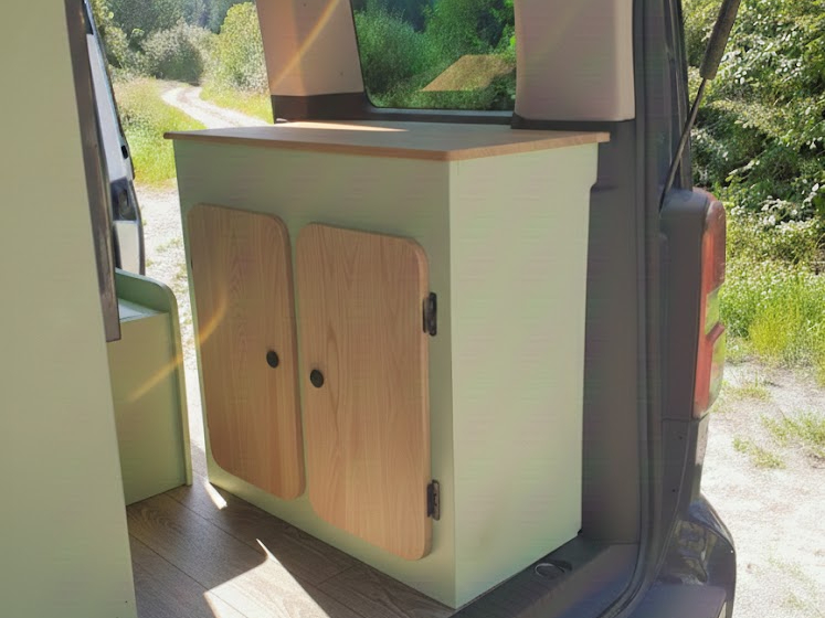 Aménagement van : meuble de rangement en bois avec vue sur une nature ensoleillée.